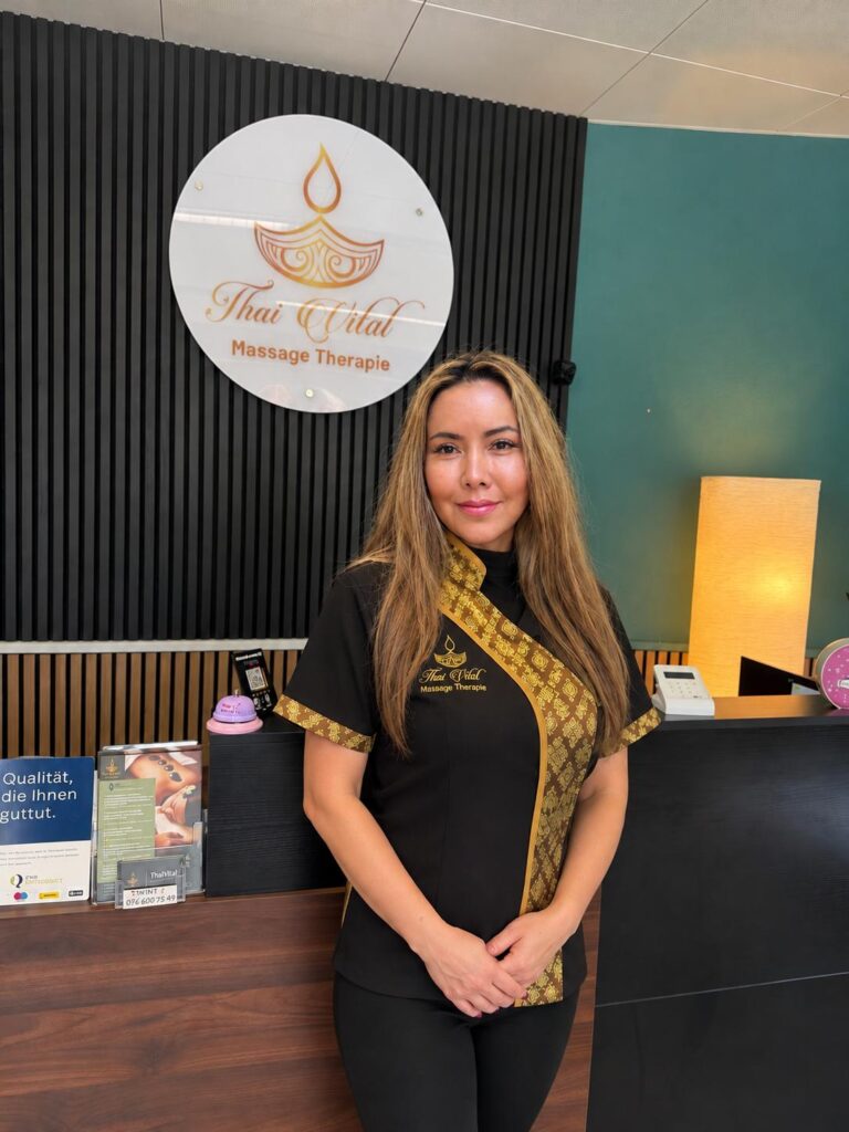 Über ThaiVital Thaimassage in Basel 1 Natcha Samphan, Inhaberin von ThaiVital, in Berufskleidung am Empfang des Massagesalons in Basel